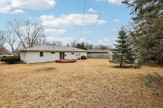 rear view of house with a deck, a yard, a chimney, and fence