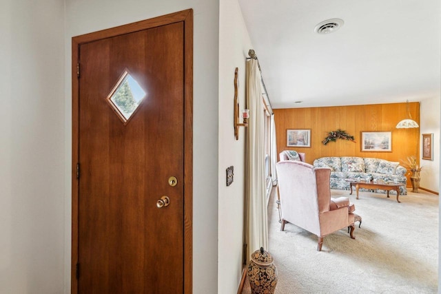 carpeted foyer with visible vents, wood walls, and baseboards