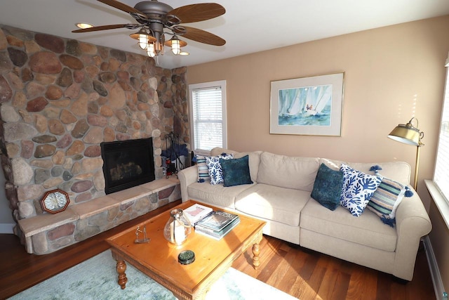 living room with a ceiling fan, a stone fireplace, and wood finished floors