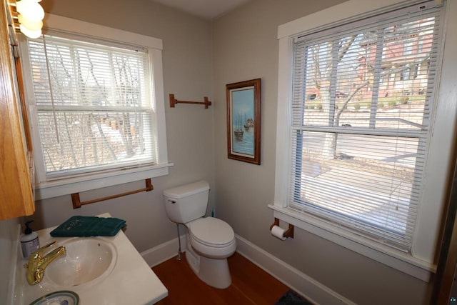 half bathroom featuring wood finished floors, a sink, toilet, and baseboards