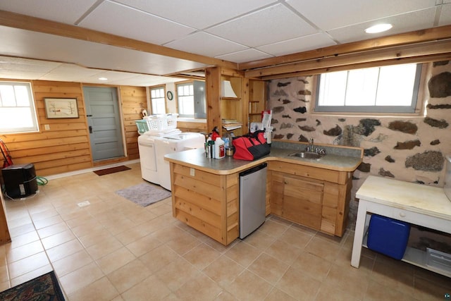 kitchen featuring a paneled ceiling, light countertops, stainless steel dishwasher, a sink, and independent washer and dryer