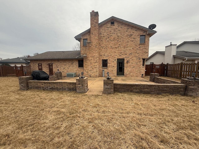 rear view of property with fence, a lawn, brick siding, and a patio area