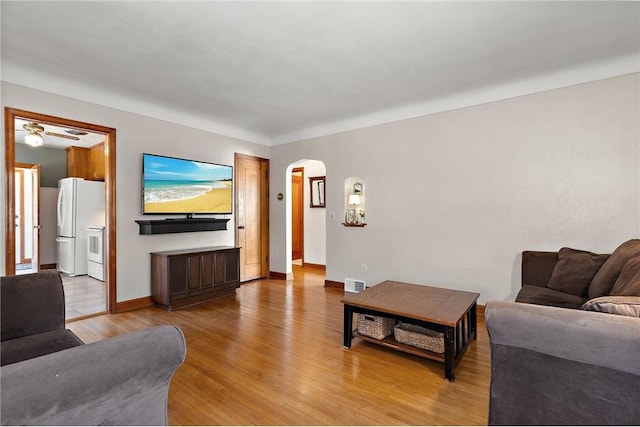 living area featuring light wood-style floors, arched walkways, visible vents, and baseboards