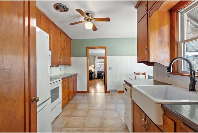 kitchen featuring white appliances, a sink, visible vents, wainscoting, and brown cabinets