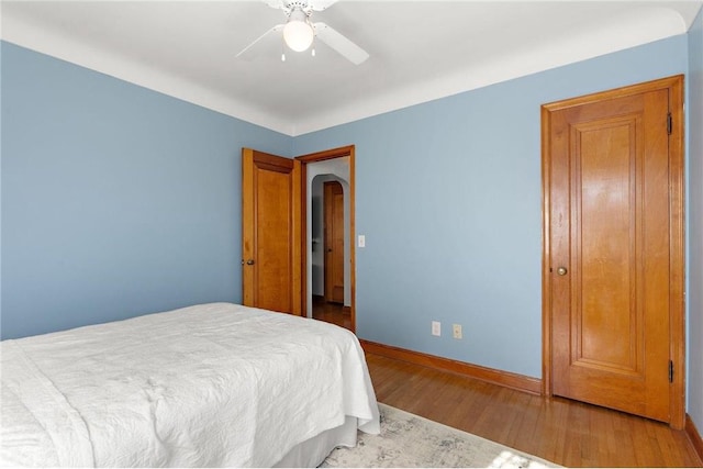 bedroom featuring a ceiling fan, baseboards, arched walkways, and wood finished floors