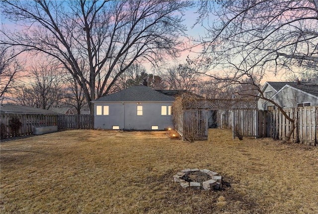 back of house at dusk with a fenced backyard, a fire pit, crawl space, a lawn, and stucco siding