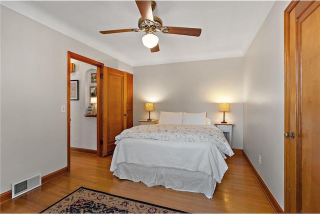 bedroom featuring a ceiling fan, visible vents, baseboards, and wood finished floors