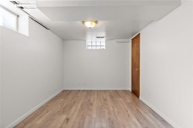 below grade area with light wood-style flooring, visible vents, and baseboards