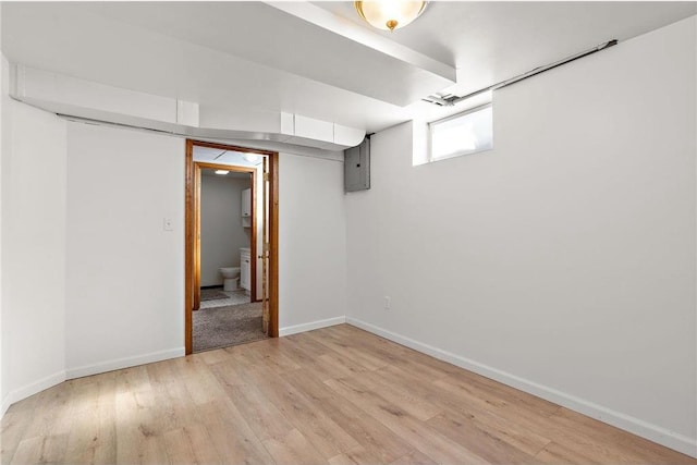 below grade area with electric panel, light wood-style flooring, and baseboards