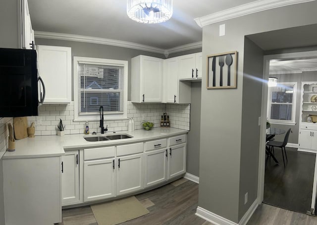 kitchen featuring dark wood-style flooring, light countertops, ornamental molding, white cabinetry, and a sink