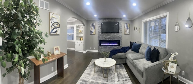 living area featuring visible vents, dark wood finished floors, arched walkways, ornamental molding, and a stone fireplace