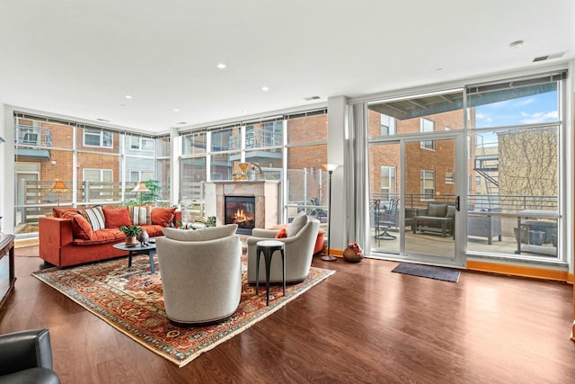 living area with a fireplace, visible vents, a wall of windows, and wood finished floors