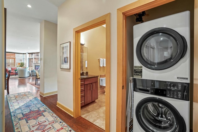 laundry room featuring recessed lighting, wood finished floors, stacked washer and clothes dryer, and baseboards