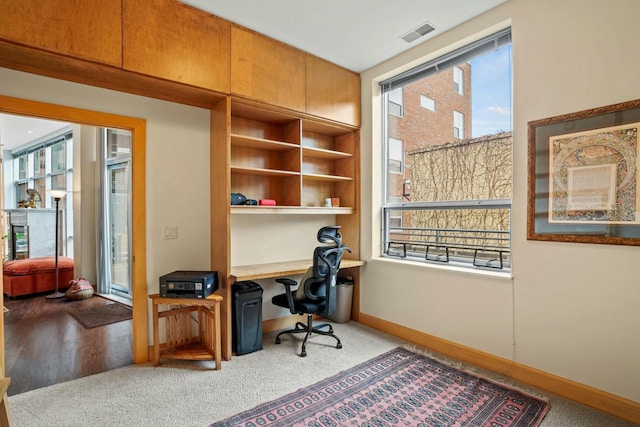 home office featuring carpet floors, a fireplace, visible vents, baseboards, and built in desk