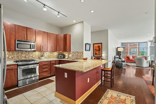 kitchen with a breakfast bar area, tasteful backsplash, appliances with stainless steel finishes, open floor plan, and a peninsula