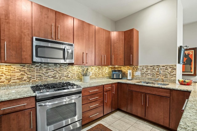 kitchen featuring tasteful backsplash, appliances with stainless steel finishes, light stone counters, and a sink