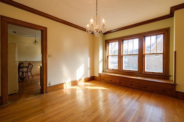 spare room featuring crown molding, light wood-style flooring, baseboards, and an inviting chandelier