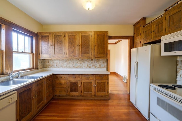 kitchen featuring dark wood-style flooring, light countertops, brown cabinetry, a sink, and white appliances