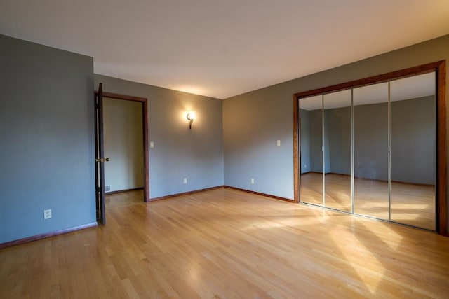 unfurnished bedroom featuring light wood-style flooring, baseboards, and a closet