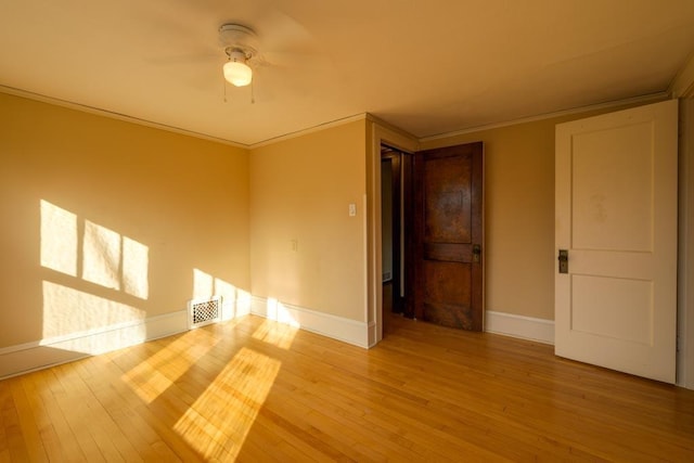 spare room with baseboards, light wood-type flooring, visible vents, and crown molding