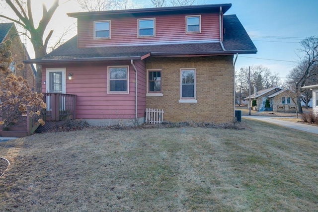 rear view of property with roof with shingles, a lawn, and brick siding