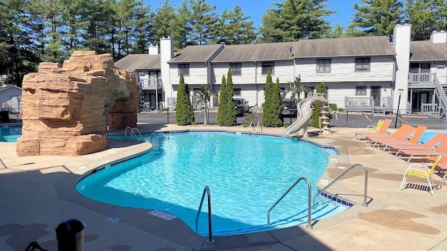 pool with a patio area, a residential view, and a water slide