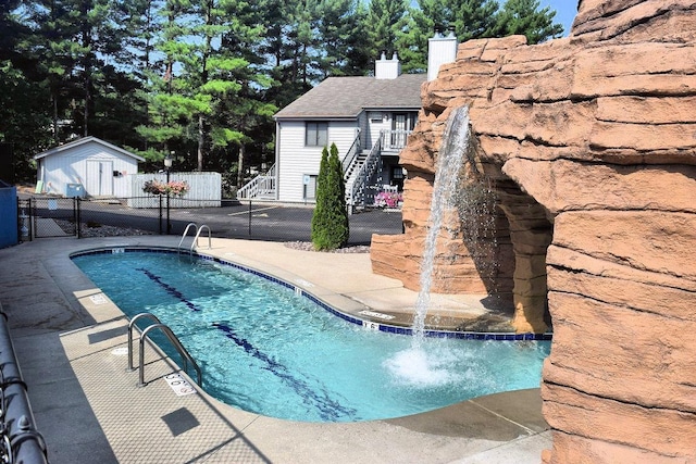 community pool featuring stairway, a patio area, fence, and an outbuilding