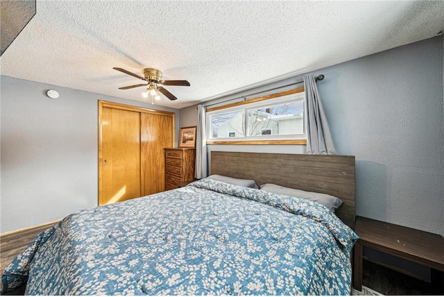 bedroom with a textured ceiling, ceiling fan, a textured wall, wood finished floors, and a closet