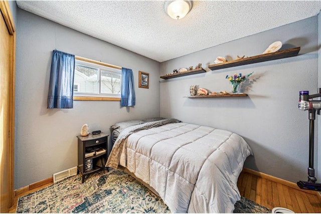 bedroom with baseboards, a textured ceiling, visible vents, and wood finished floors