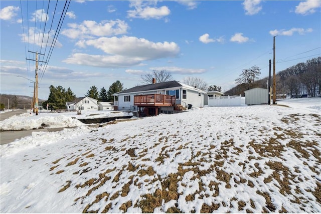 snow covered house featuring an outbuilding, fence, and a deck