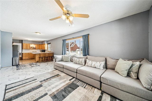 living room with marble finish floor, ceiling fan, and a textured ceiling