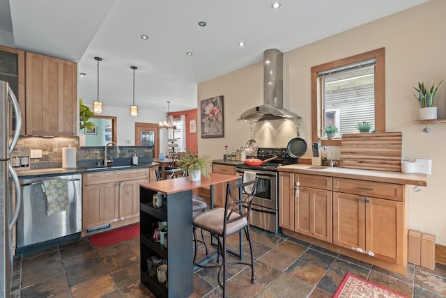 kitchen with appliances with stainless steel finishes, stone tile flooring, a sink, and wall chimney exhaust hood