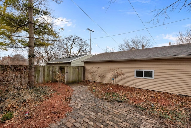 view of home's exterior with a shingled roof, a patio area, and fence