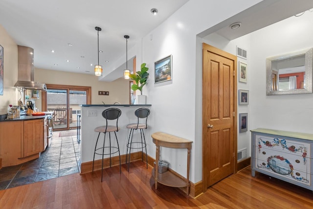 kitchen with a kitchen breakfast bar, wood-type flooring, visible vents, and island range hood