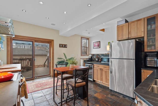 kitchen with dark countertops, stone tile flooring, recessed lighting, freestanding refrigerator, and beverage cooler