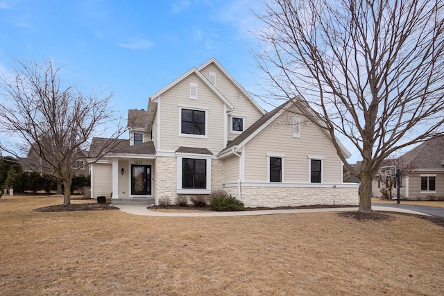 traditional-style home with stone siding, a shingled roof, and a front lawn