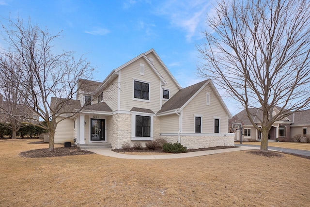 traditional-style house with stone siding, a front lawn, and a shingled roof