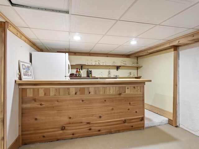 bar with a drop ceiling, freestanding refrigerator, and finished concrete floors