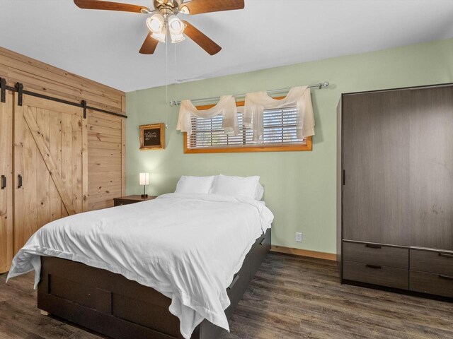 bedroom featuring a barn door, ceiling fan, baseboards, and wood finished floors