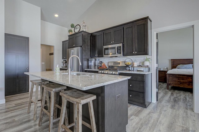 kitchen featuring tasteful backsplash, appliances with stainless steel finishes, a kitchen bar, high vaulted ceiling, and a sink