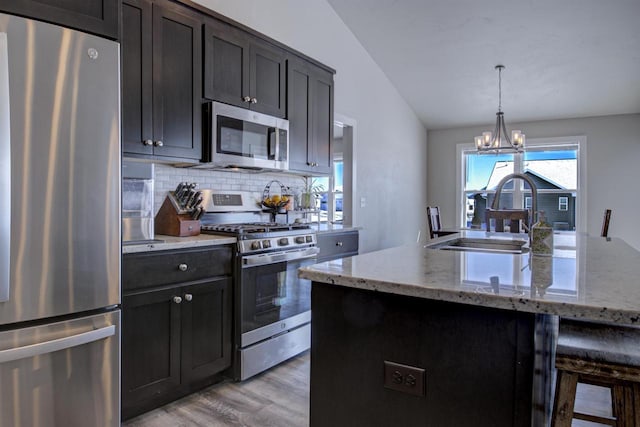 kitchen with lofted ceiling, stainless steel appliances, a sink, decorative backsplash, and light wood finished floors