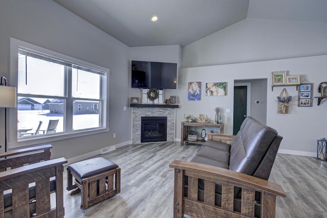 living area with lofted ceiling, visible vents, a stone fireplace, wood finished floors, and baseboards