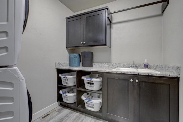 laundry room with light wood-style flooring, a sink, baseboards, stacked washer / drying machine, and cabinet space