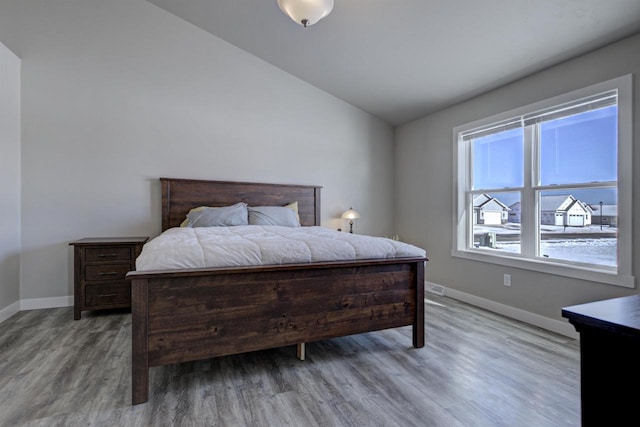 bedroom with vaulted ceiling, baseboards, and wood finished floors