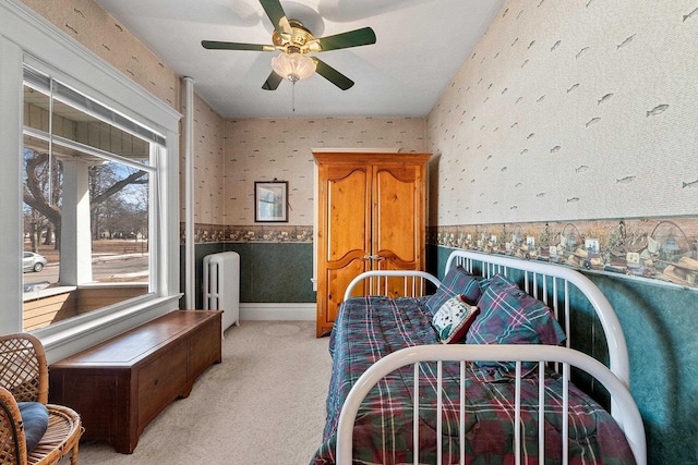 bedroom featuring wallpapered walls, ceiling fan, a wainscoted wall, and light colored carpet