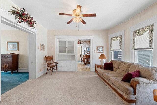 living area featuring ceiling fan, baseboards, and light colored carpet