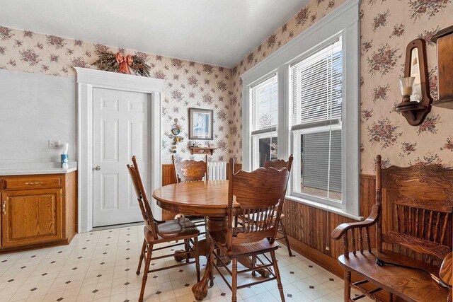 dining room with light floors, wainscoting, and wallpapered walls