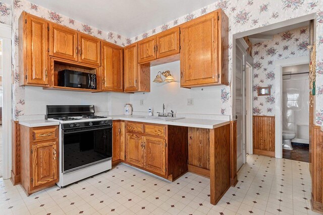 kitchen with black microwave, a wainscoted wall, light floors, gas range oven, and wallpapered walls