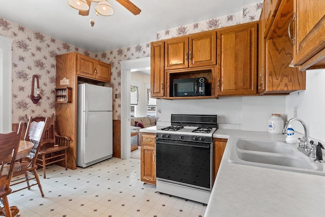 kitchen featuring gas range oven, freestanding refrigerator, a sink, black microwave, and wallpapered walls