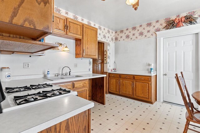 kitchen featuring brown cabinetry, a sink, and wallpapered walls